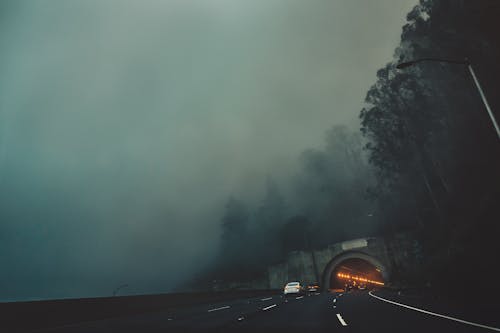 Cars riding along asphalt road towards tunnel on gloomy weather