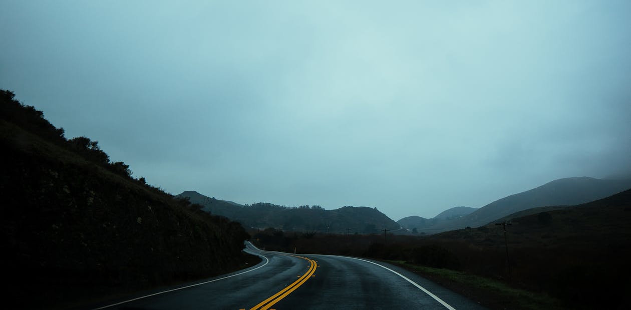 Curvy asphalt roadway going amidst green lush hills in highlands on haze day