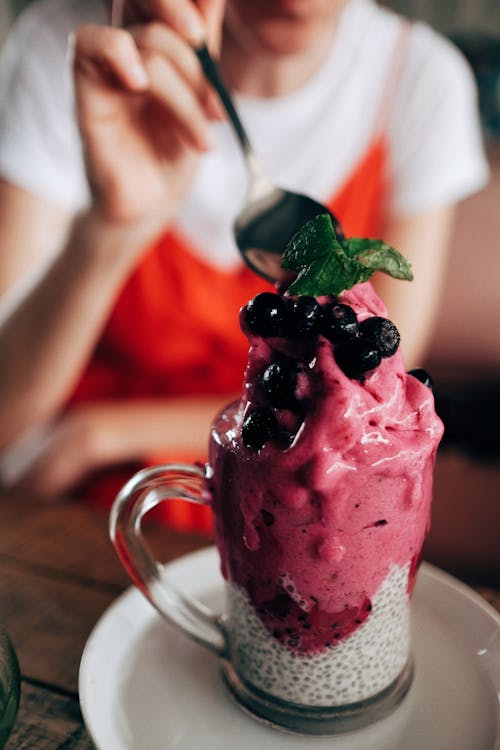 Free Crop anonymous lady enjoying appetizing healthy smoothie dessert with chia seeds dragon fruit and blueberries sitting at table in cafe Stock Photo