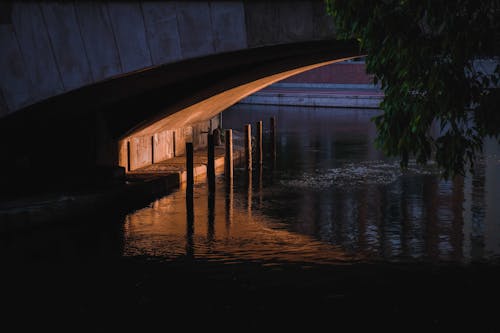 Narrow space and enclosure under concrete bridge over calm rippling river in dusk