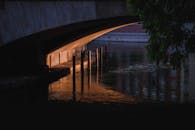 Narrow space and enclosure under concrete bridge over calm rippling river in dusk