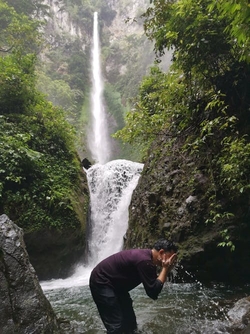 Unrecognizable tourist washing face with creek water near fast cascade