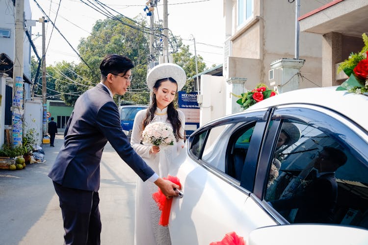 Stylish Asian Groom Opening Car Door To Elegant Bride