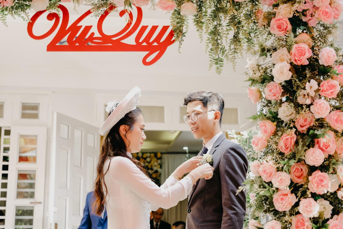 Asian bride putting flower decor on jacket of groom · Free Stock Photo