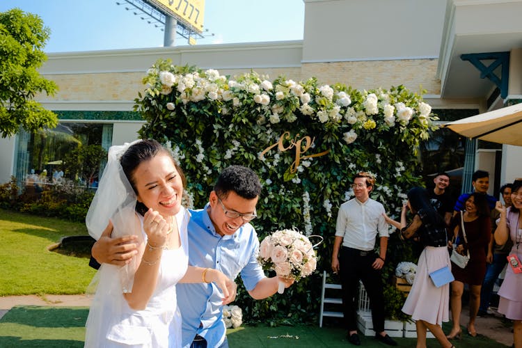 Excited Asian Newlywed Couple Laughing Behind Visitors