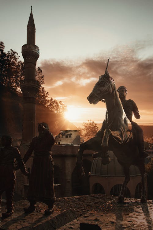 Free Low angle of aged masonry statues of horse and men near tower under cloudy sky at colorful sunset in evening Stock Photo