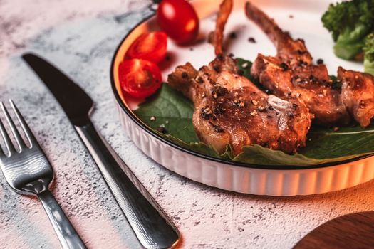 Grilled pork chops garnished with tomatoes and greens on plate with cutlery.