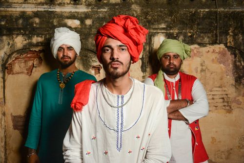Free Serious ethnic male friends in bright clothes and head wear looking at camera while standing near dirty shabby wall Stock Photo