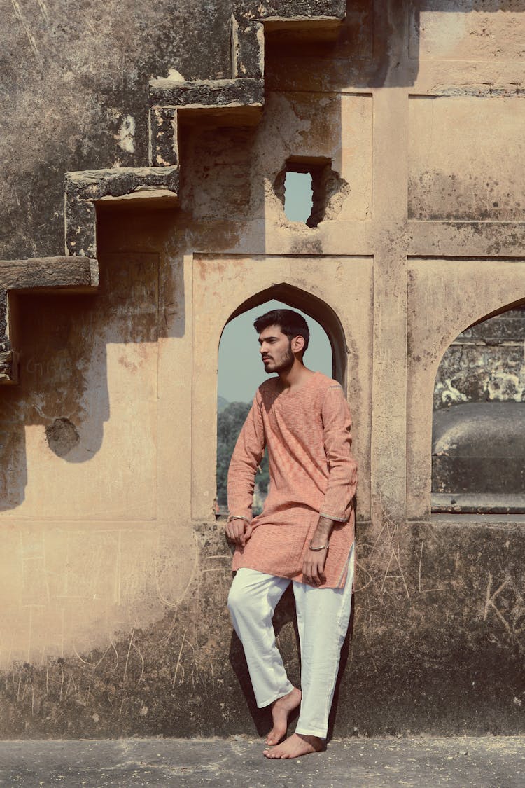 Barefoot Ethnic Man In Traditional Clothes Near Old Street Wall