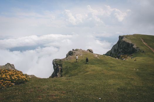 Person Standing on Green Grass Field Near Gray Rock Formation Under White Clouds