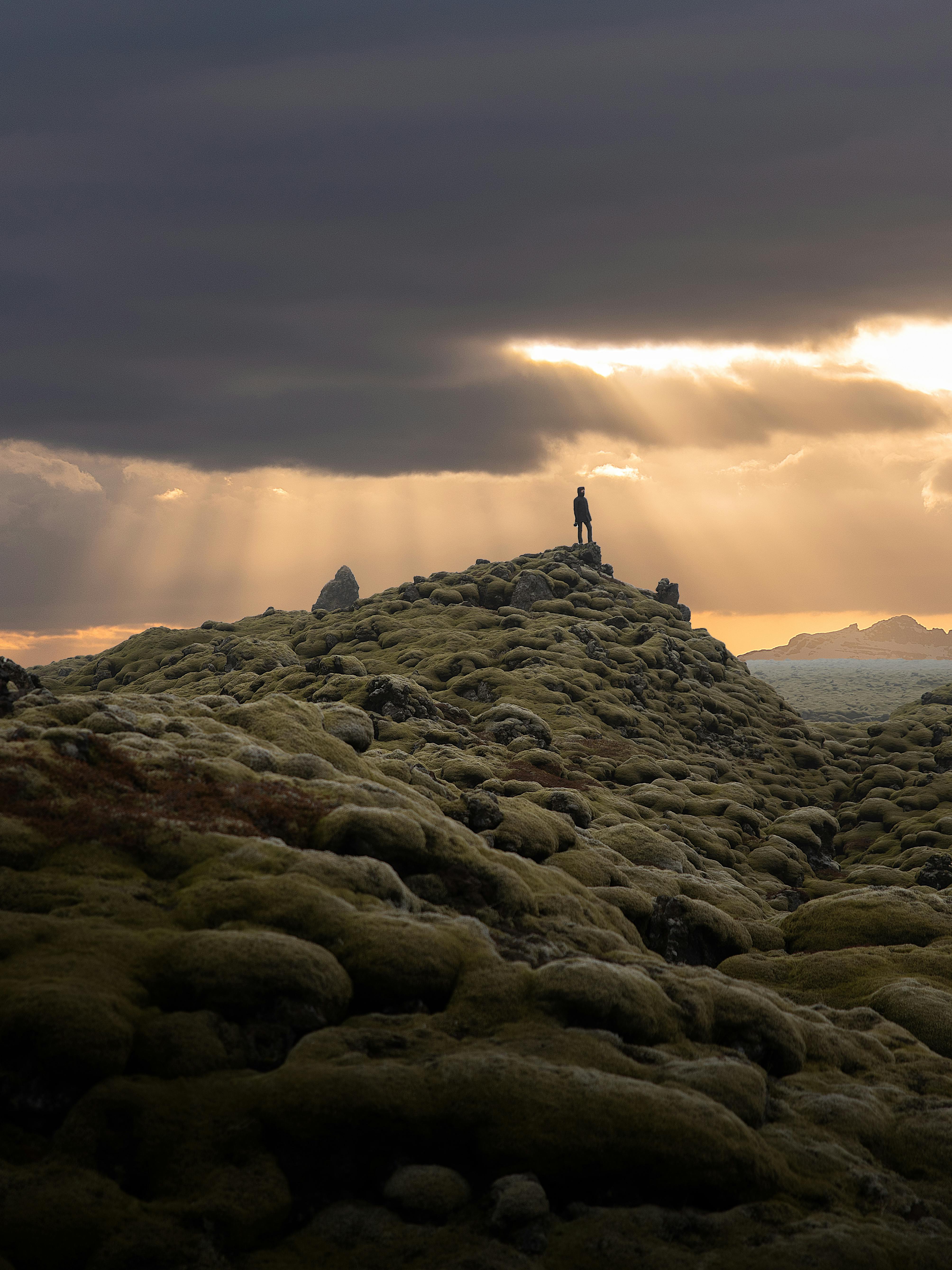 person standing on rocky hill during sunset