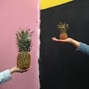 Two People Holding Pineapple Fruits Against a Multicolored Wall