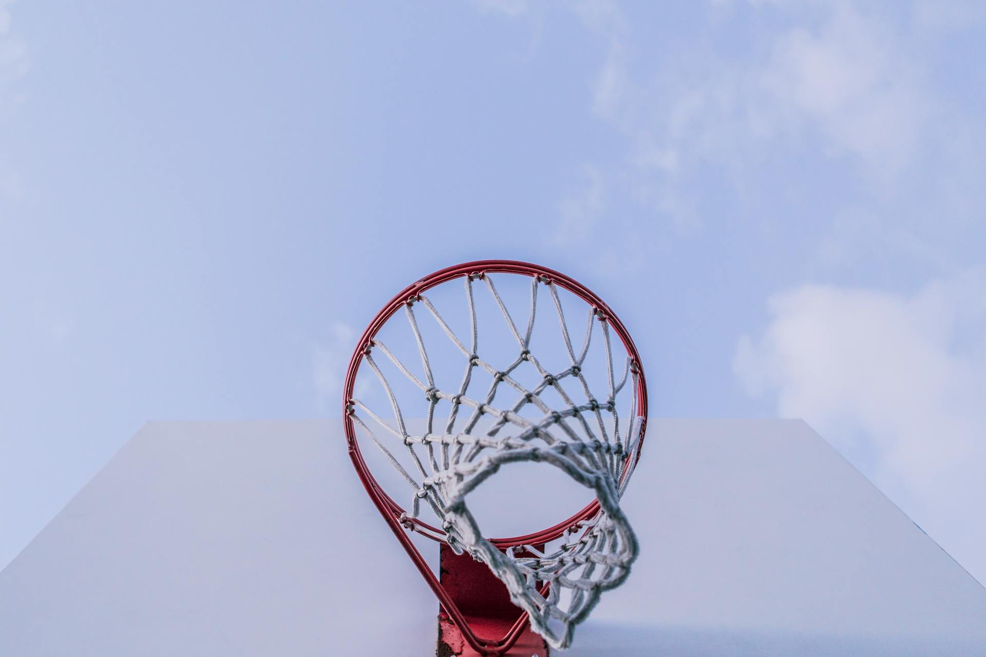 A dynamic low-angle view of a basketball hoop with a clear blue sky backdrop, capturing the essence of outdoor sports.