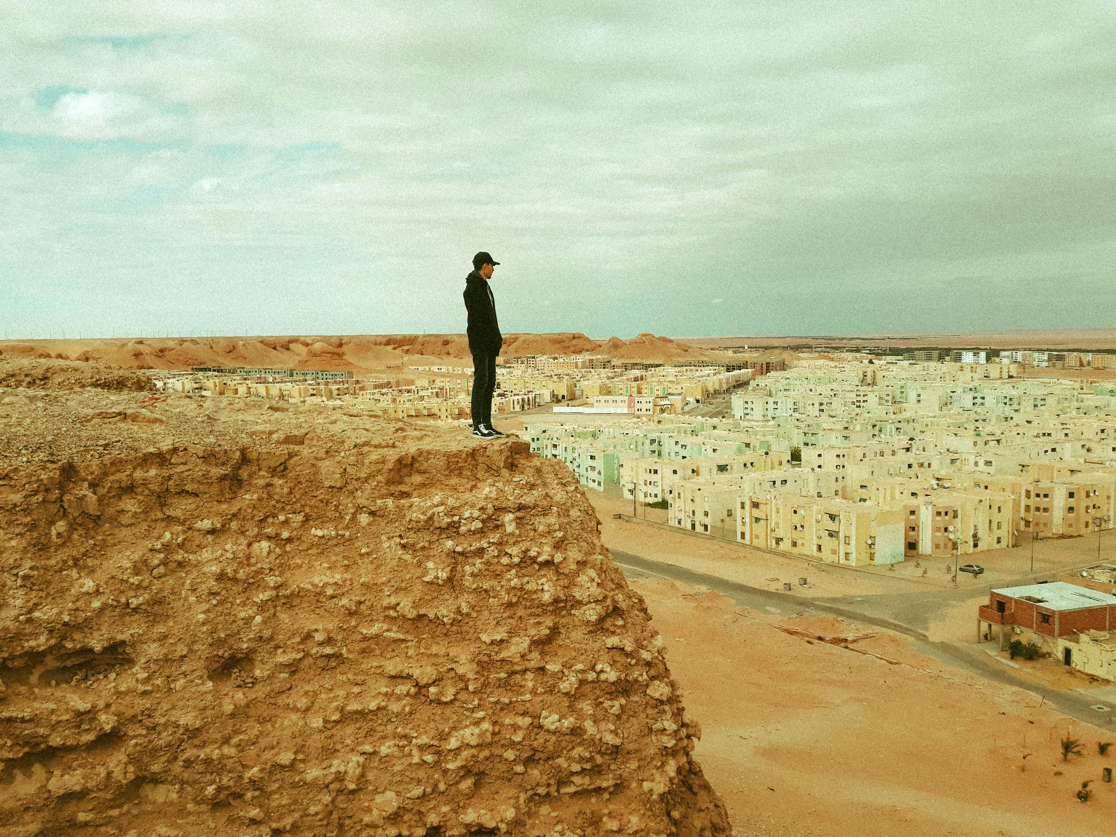 Man standing on a cliff edge overlooking the desert town of Ouargla, Algeria.
