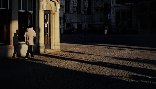 A lone figure walks through Leuven's dramatic cobblestone streets, casting long shadows.