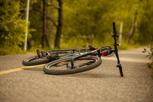 Free Ground level of modern bicycle lying on shabby road near green trees in summertime Stock Photo