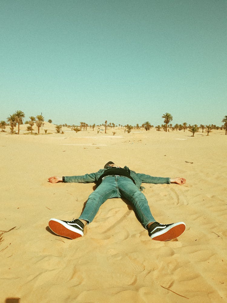 Man In Blue Denim Jacket And Jeans Lying Down On Desert Sand