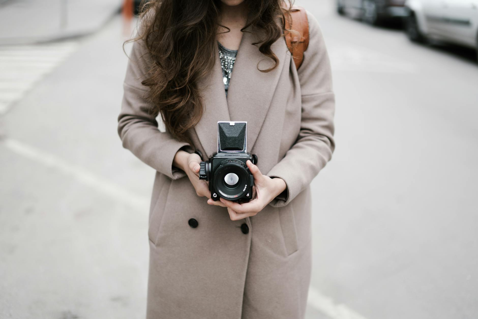 A fashionable woman in a coat holds a vintage camera in an urban setting, embodying casual street photography.