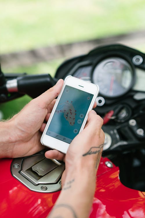 Free From above of crop anonymous tattooed male holding smartphone while studying map of island via Internet sitting on motorbike on street Stock Photo