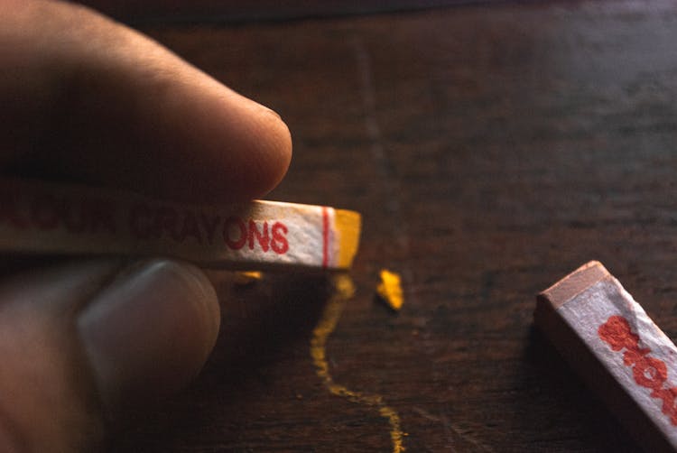 Person Holding Yellow Crayon Writing On Wooden Surface