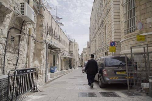 Man Walking on the Street Between Buildings with Stonewalls