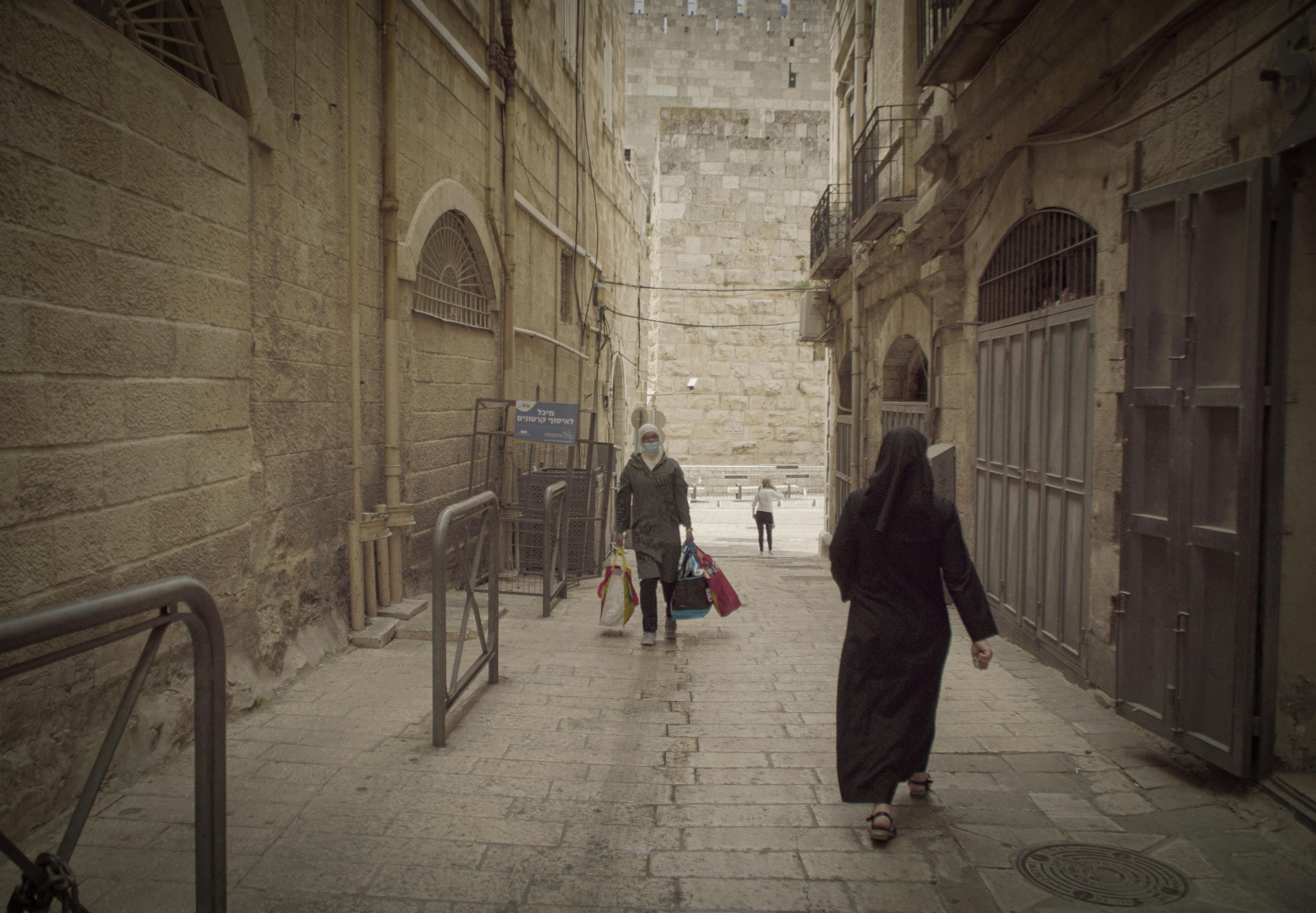 People walking through a narrow alleyway in Jerusalem Old City, showcasing historic architecture.