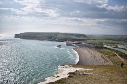 Picturesque shining endless sea with rippled water near grass mounts under sky with clouds