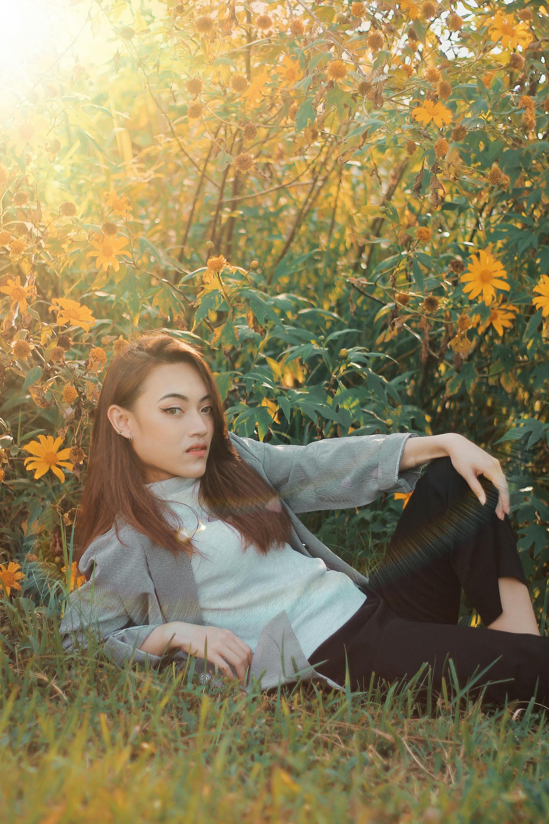 一位时尚的年轻女子懒洋洋地躺在阳光明媚的黄色花丛中，散发着宁静而自信的气息