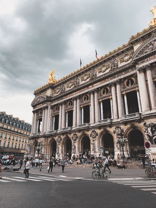Free Tourists gather at the iconic Palais Garnier in Paris under a dramatic sky, capturing its historic elegance. Stock Photo