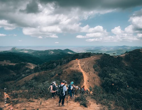 People Hiking on Brown Mountain Under White Clouds and Blue Sky