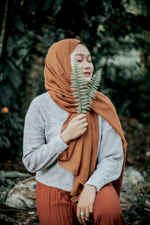 Happy young ethnic female enjoying smell of fresh plant in park