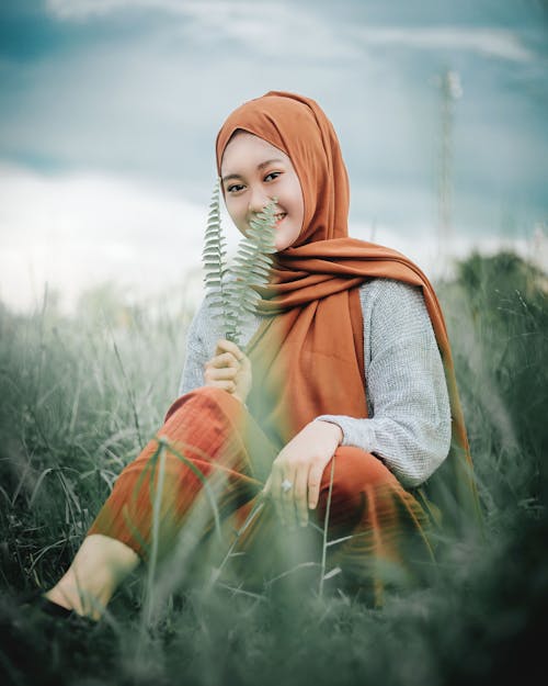 Cheerful young Muslim lady relaxing in green field