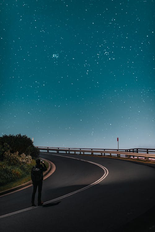 Anonymous tourist taking photo of starry sky while standing on road