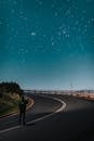 Anonymous tourist taking photo of starry sky while standing on road