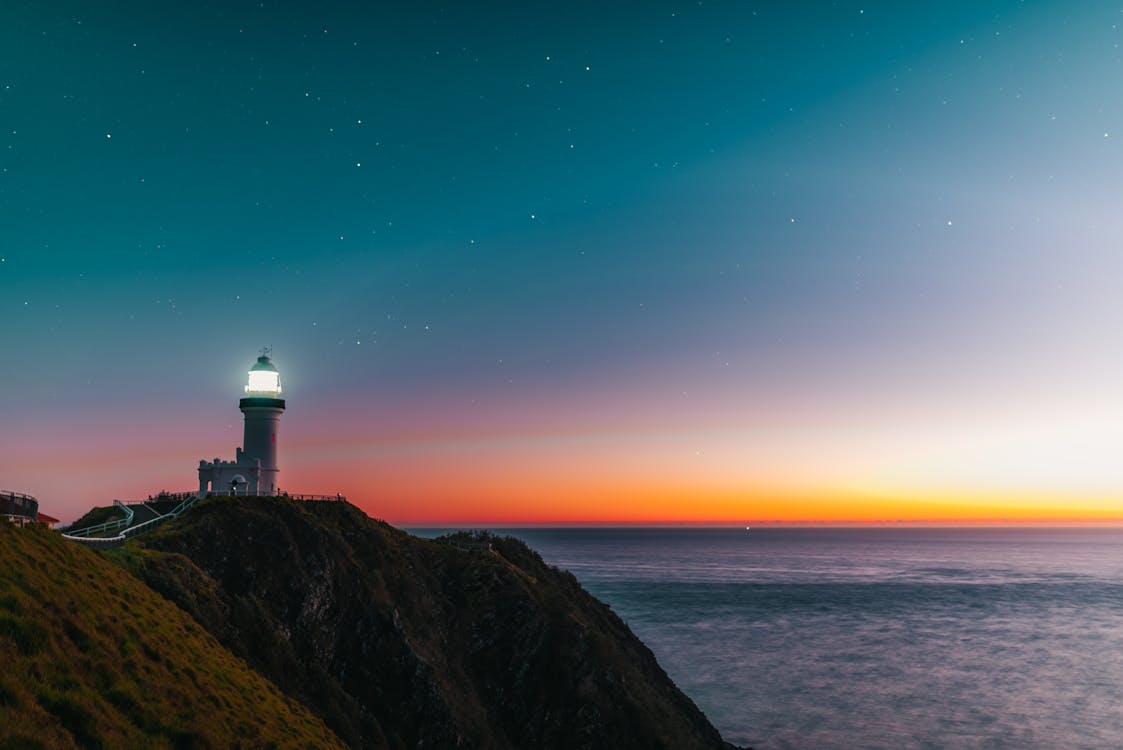 Free Amazing scenery of lighthouse tower located on rocky cliff against starry sunset sky over wavy ocean Stock Photo