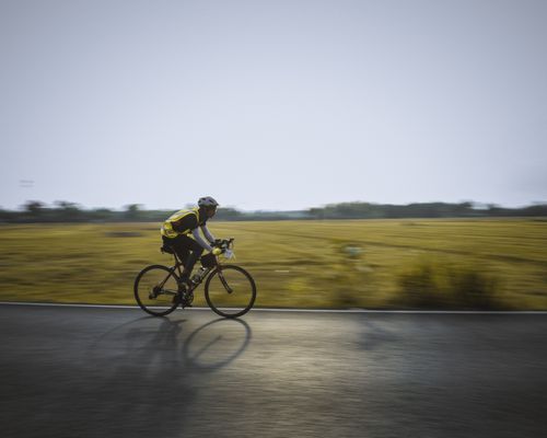 Free Side view of unrecognizable male cyclist in helmet riding bike on asphalt road near green grassy field on sunny day Stock Photo