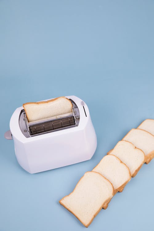 High angle of white modern toaster placed on blue background with bread slices