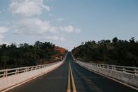 Gray Concrete Road Between Green Trees Under White Clouds and Blue Sky
