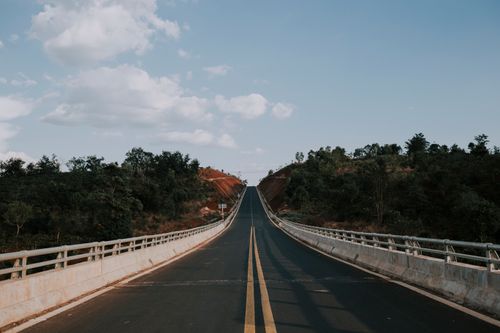 Free Long highway bridge with a perspective under a blue sky and fluffy clouds, surrounded by nature. Stock Photo