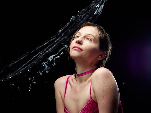 Free Attractive female in pink wear and choker with wet hair against dark background with water splashing above head Stock Photo