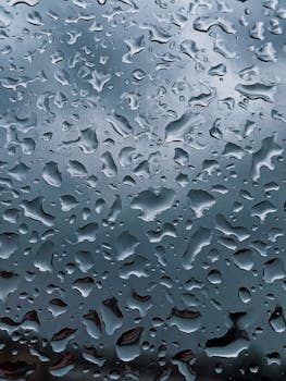 Close-up of raindrops on a glass window with a gloomy sky in the background, creating an abstract pattern.