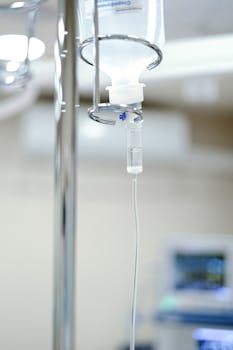 Close-up view of an IV drip chamber and stand in a clinical hospital environment.