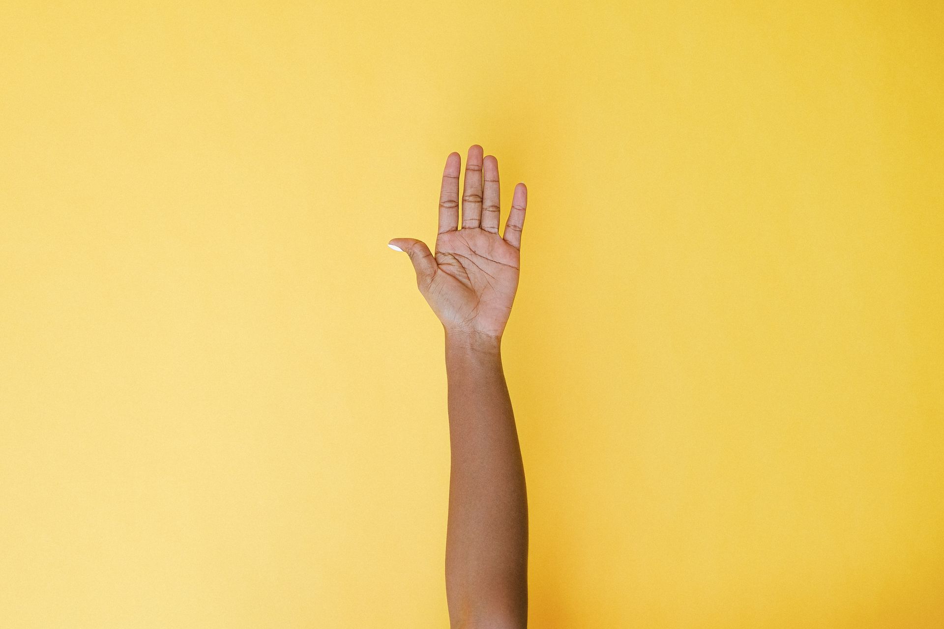 A hand raised against a vibrant yellow background, symbolizing help or volunteering.