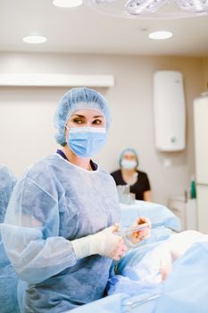 在医院手术室里，一名身穿蓝色手术服、戴着口罩的女外科医生正在做手术