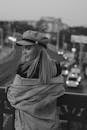 Grayscale Photo of Woman in Jacket and Hat Standing beside Handrail