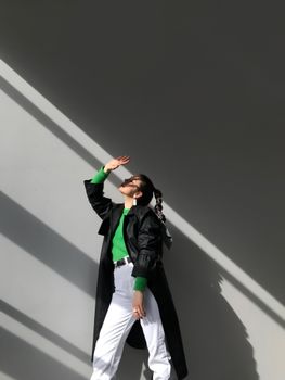 阳光下，一位身穿绿色上衣和深色外套的时尚女性，捕捉着现代城市风格