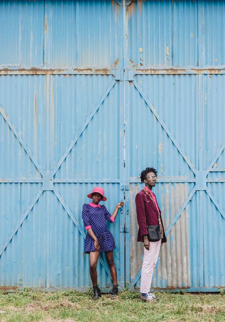Full body of stylish African American couple wearing cool clothes standing against rusty metal gates