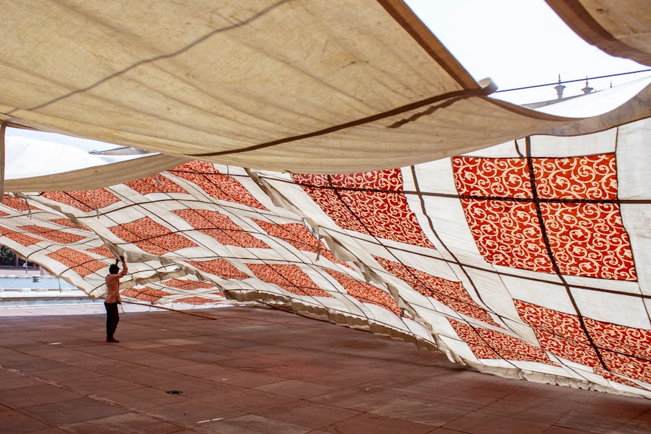 A person adjusting a large decorative canopy with red patterns in an outdoor space.