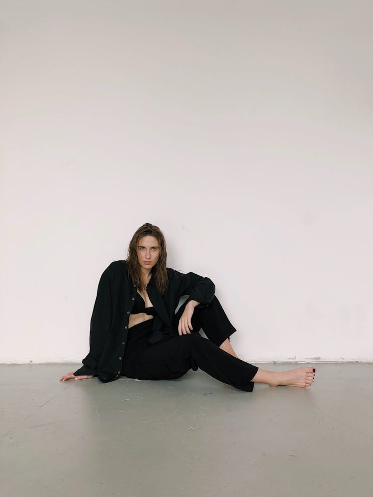 Barefoot Woman In Black Sitting By Wall