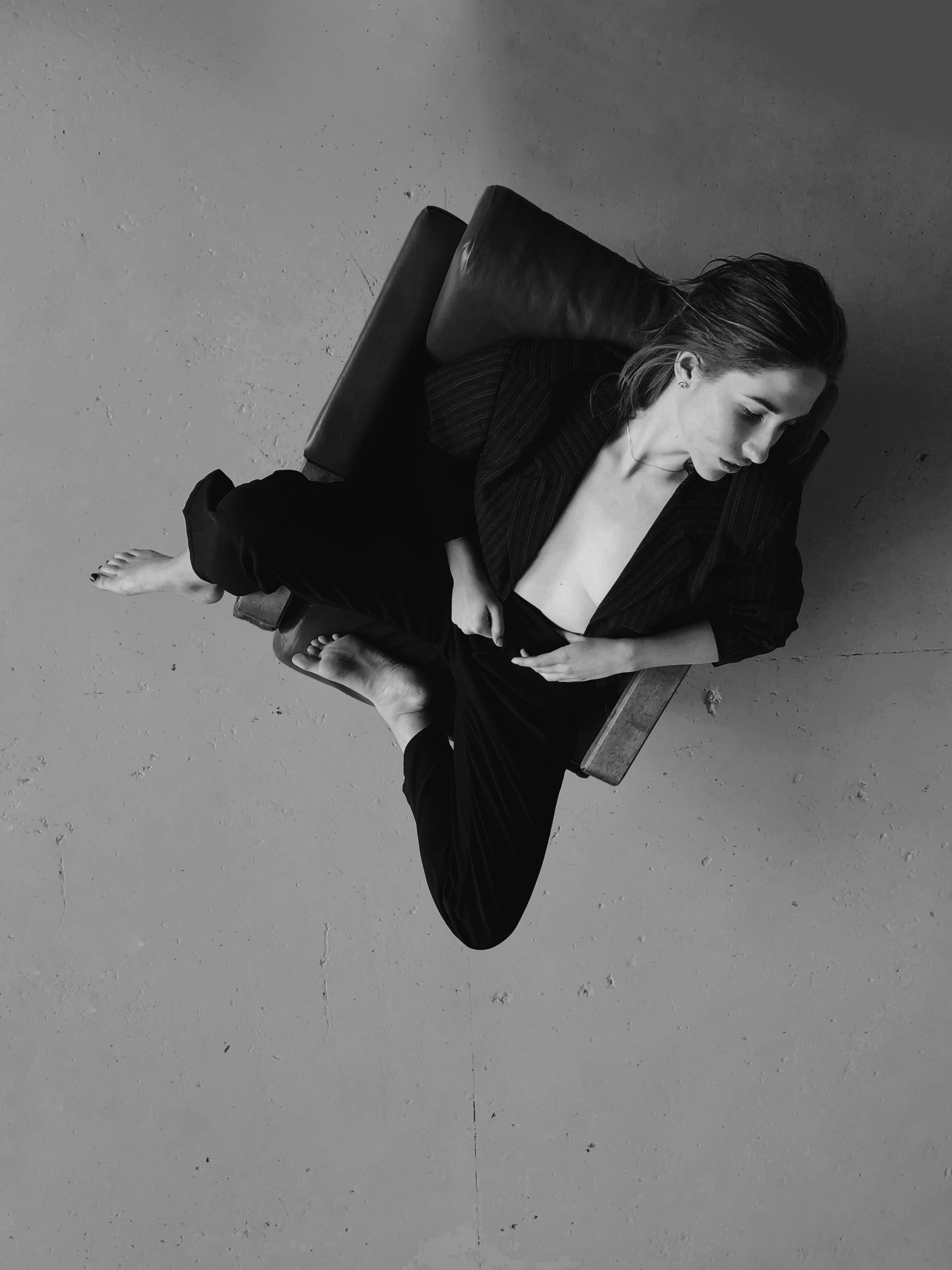Elegant black and white portrait of a woman in a blazer posing gracefully on an armchair.